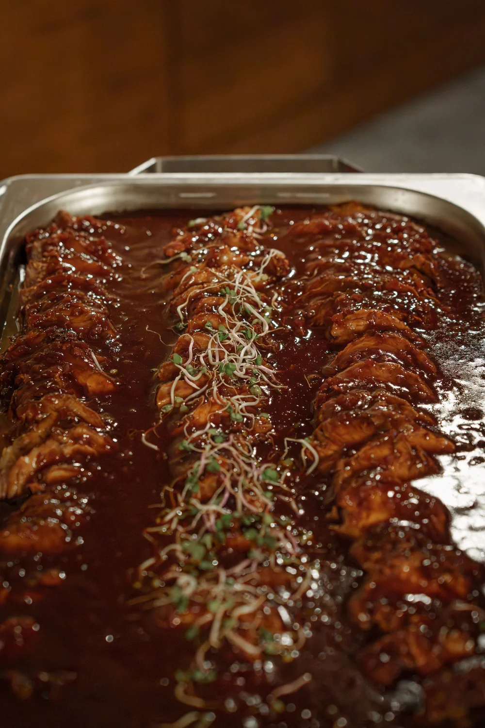 Königliche Schlossgastronomie – Dieses Bild zeigt ein Gericht aus glasiertem Fleisch, wahrscheinlich Schweinerippchen oder Hühnchen in einer dicken, dunklen Barbecue-Sauce, serviert in einer großen Catering-Chafer-Dish aus Edelstahl.