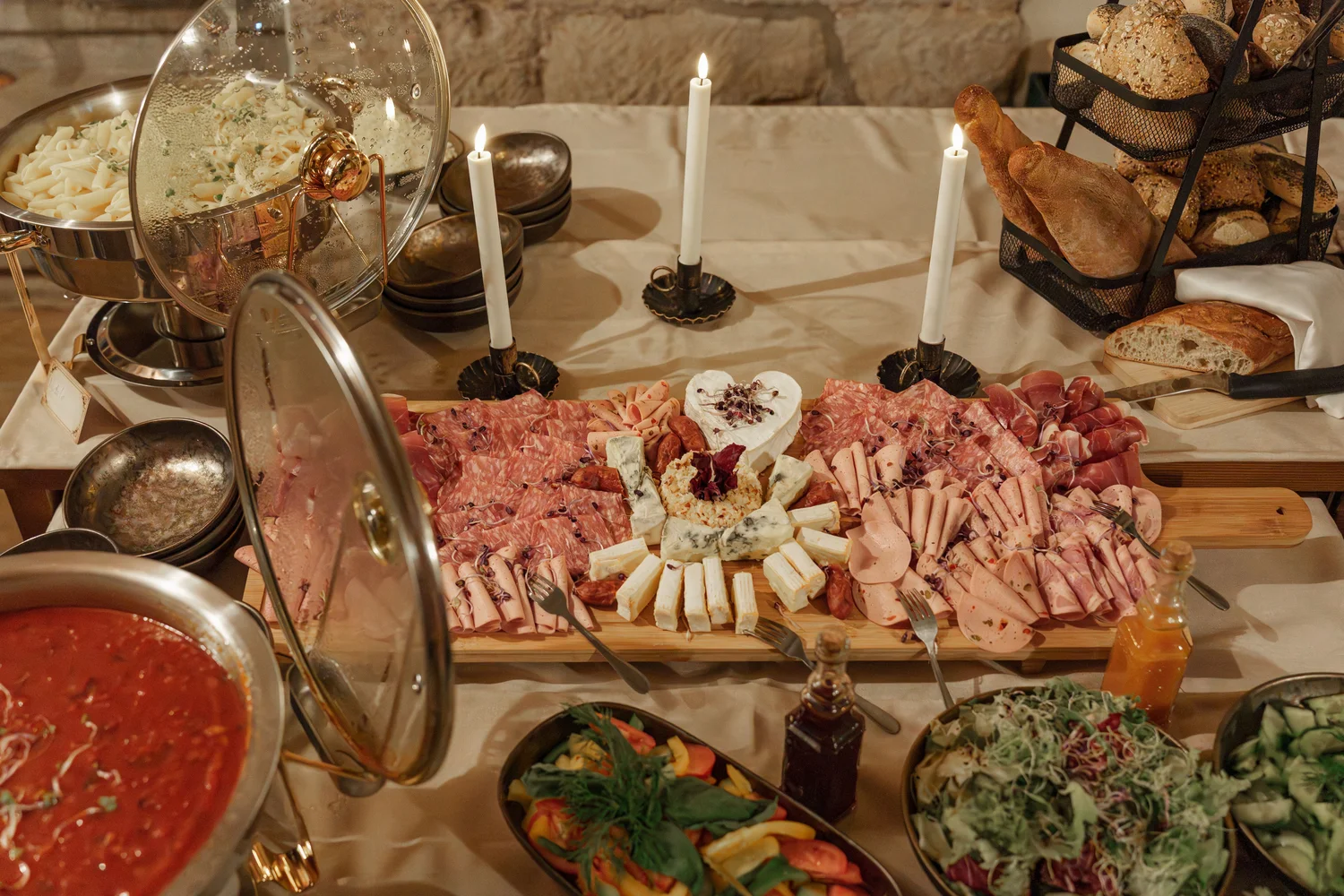 Königliche Schlossgastronomie – Das Bild zeigt ein Buffet mit einer Vielzahl von Gerichten, darunter warme Speisen in Warmhaltebehältern, frische Salate und eine Platte mit verschiedenen Fleisch- und Käsesorten.