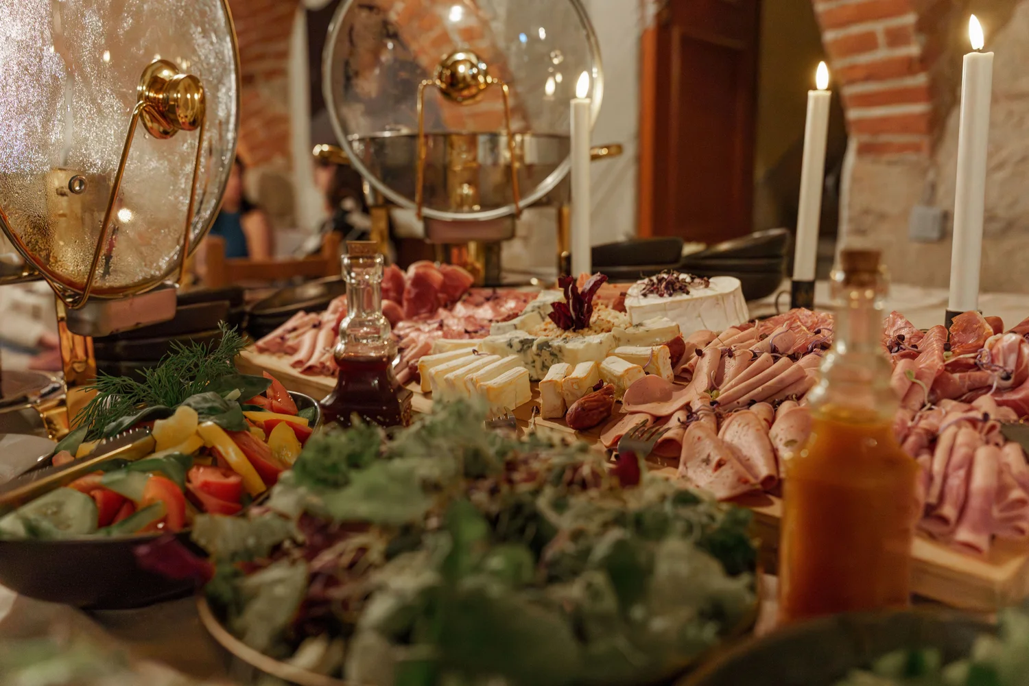Königliche Schlossgastronomie – Das Bild zeigt ein Buffet mit einer Vielzahl von Gerichten, darunter warme Speisen in Warmhaltebehältern, frische Salate und eine Platte mit verschiedenen Fleisch- und Käsesorten.