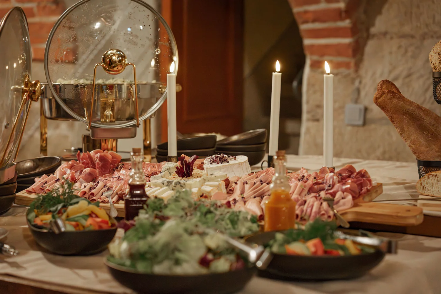 Königliche Schlossgastronomie – Das Bild zeigt ein Buffet mit einer Vielzahl von Gerichten, darunter warme Speisen in Warmhaltebehältern, frische Salate und eine Platte mit verschiedenen Fleisch- und Käsesorten.