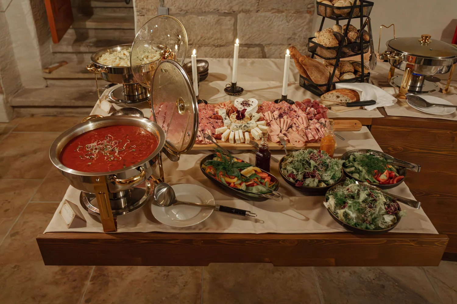 Königliche Schlossgastronomie – Das Bild zeigt ein Buffet mit einer Vielzahl von Gerichten, darunter warme Speisen in Warmhaltebehältern, frische Salate und eine Platte mit verschiedenen Fleisch- und Käsesorten.