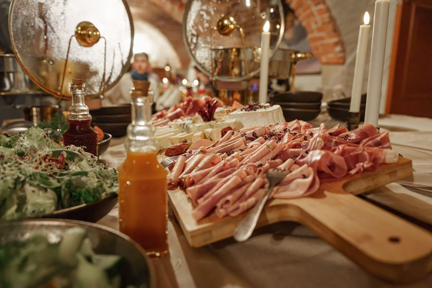 Königliche Schlossgastronomie – Das Bild zeigt ein Buffet mit einer Vielzahl von Gerichten, darunter warme Speisen in Warmhaltebehältern, frische Salate und eine Platte mit verschiedenen Fleisch- und Käsesorten.
