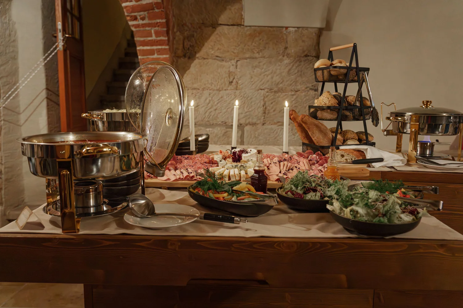 Königliche Schlossgastronomie – Das Bild zeigt ein Buffet mit einer Vielzahl von Gerichten, darunter warme Speisen in Warmhaltebehältern, frische Salate und eine Platte mit verschiedenen Fleisch- und Käsesorten.